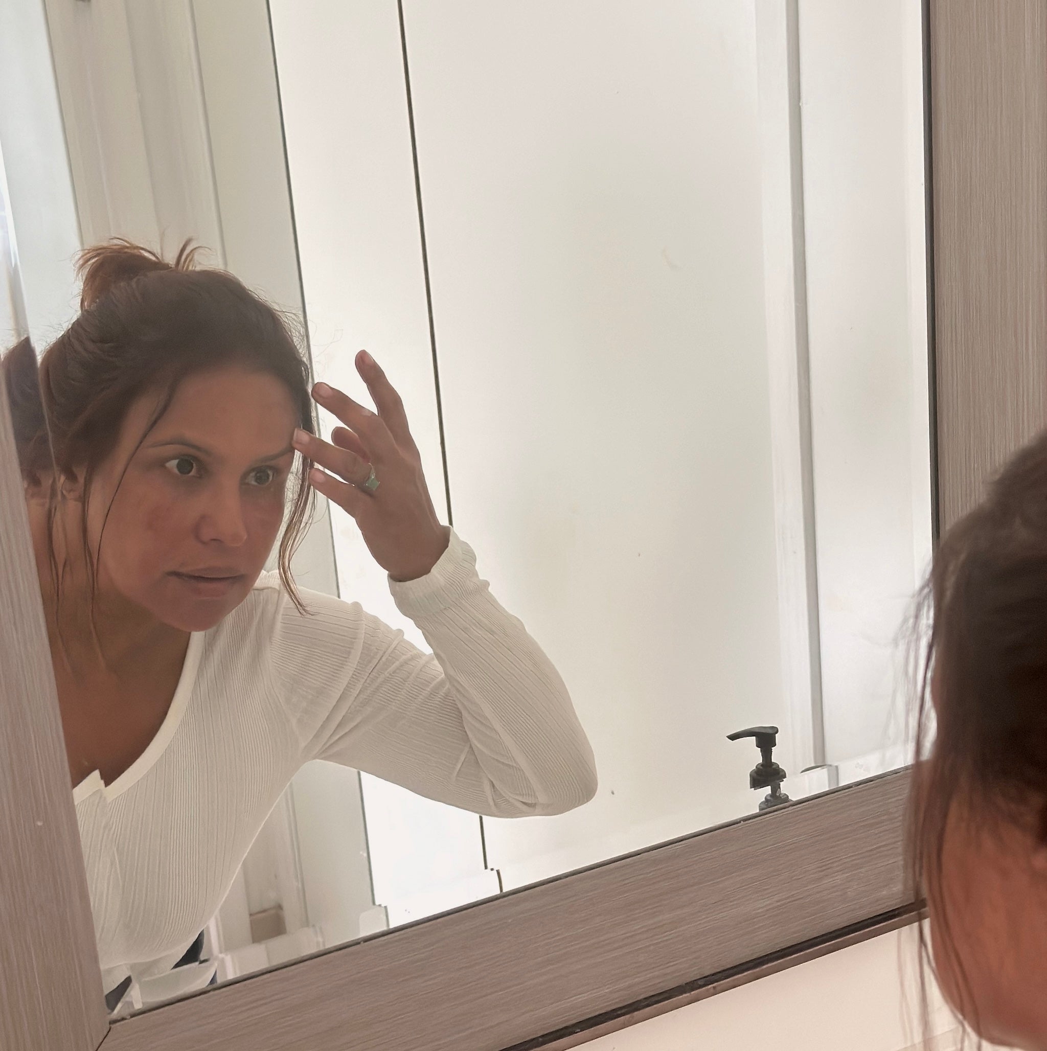 35+ year woman looking at skin in mirror feeling discouraged about her skin. Ready to take Gunilla Eisenberg's Better than Botox Pro-aging skincare course for lasting skin confidence.