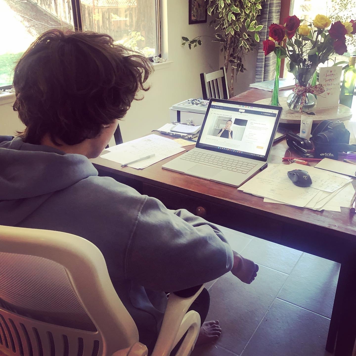 A teenage boy is seen looking at a computer screen with the digital online course 4 Weeks to better skin. He is taking notes on how to take care of his skin.