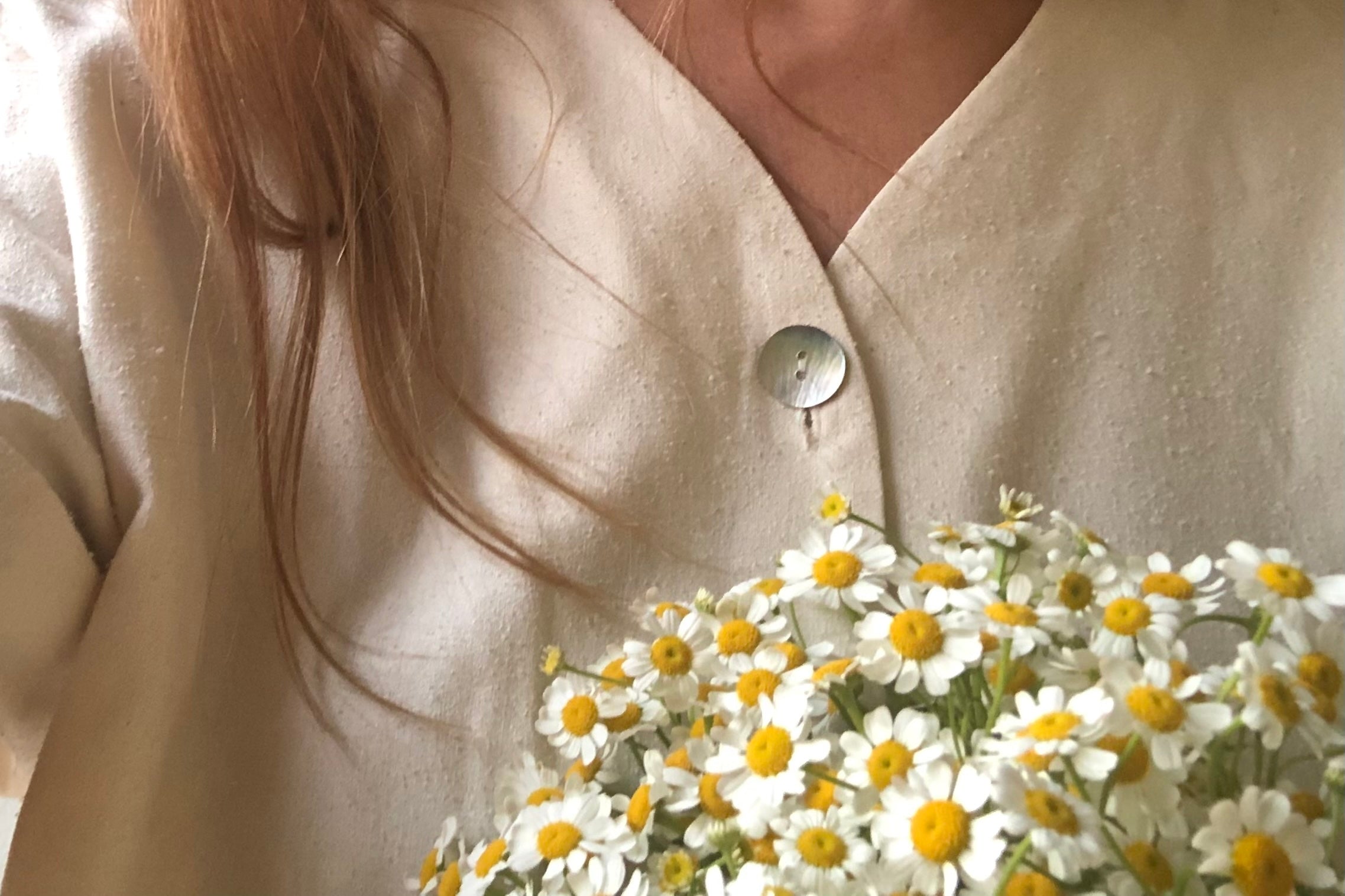 close up of a girl holding a bouquet of fresh chamomile flowers for blog about skin benefits from using chamomile ingredients in skincare and as a tea.
