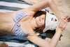 Girl is seen lying on the beach in her bikini, wearing a hat to protect her skin from sun damage and and is smiling.